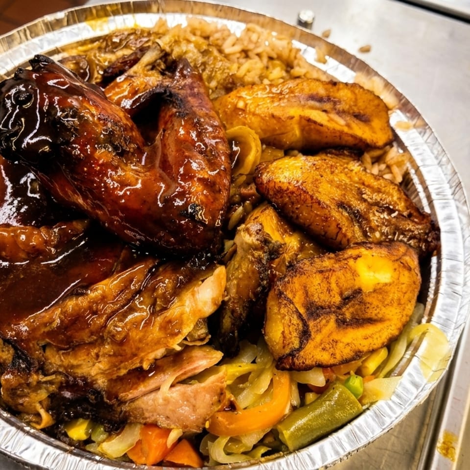 Aluminum takeout tray piled with glazed grilled chicken, fried plantains, rice, and sautéed mixed vegetables.